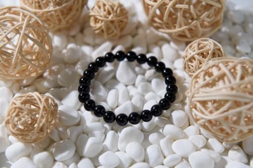 Bracelet en perles noires sur des galets blancs avec boules en rotin.